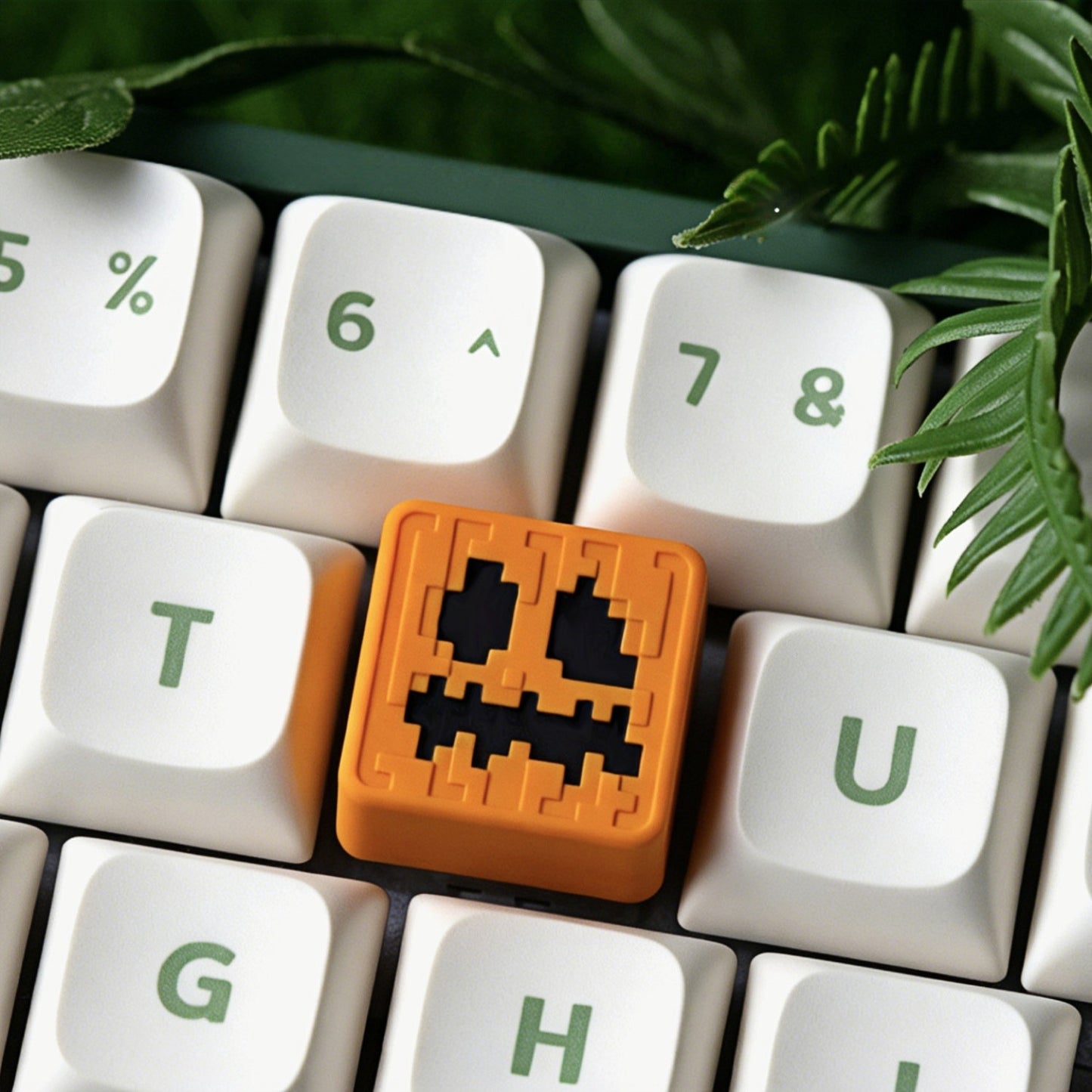 Keycapper™ Minecraft Cube Series Artisanal Keycap – A detailed 3D voxel-style Jack-o'-Lantern head novelty keycap, glowing orange with pixelated facial features, installed on a white mechanical keyboard 'T' key, surrounded by foliage.