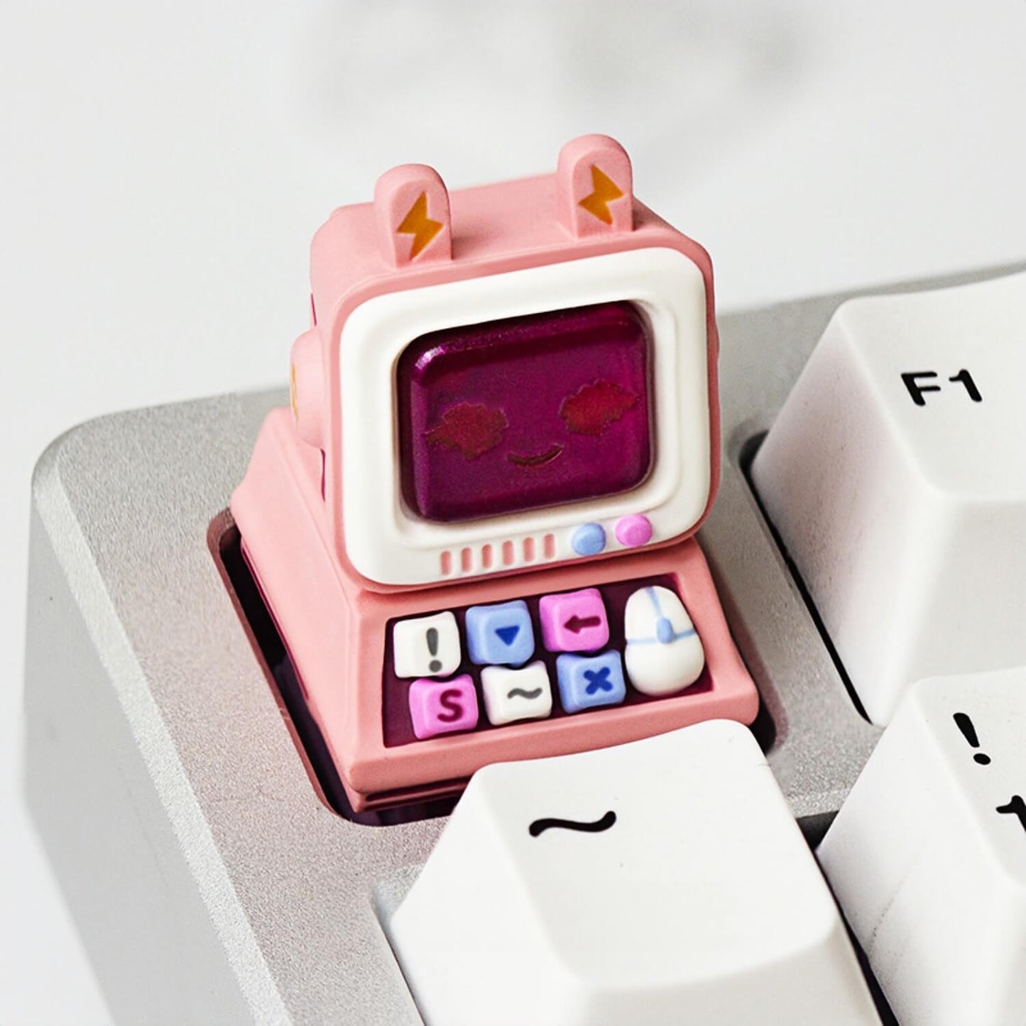 A cute pink retro computer resin keycap by Keycapper placed on the ESC key of a silver mechanical keyboard setup.