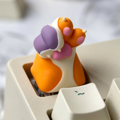 Keycapper orange calico cat paw resin artisan keycap with cute pink pads installed on a beige mechanical keyboard.