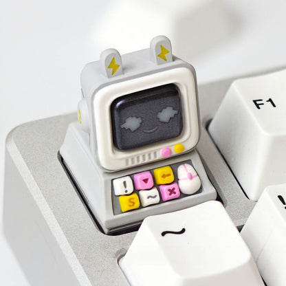 A light grey mini monitor handmade resin keycap by Keycapper with a pixel-art smiling face, mounted on a custom mechanical keyboard.