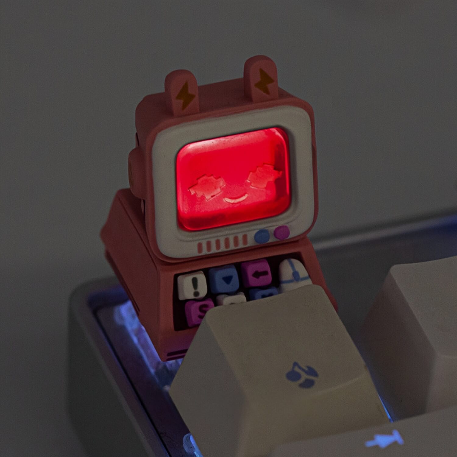 A pink mini monitor artisan keycap by Keycapper glowing with a vivid red LED backlight in a dim-lit gaming setup.