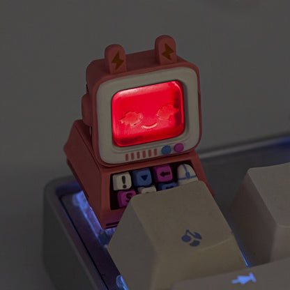 A pink mini monitor artisan keycap by Keycapper glowing with a vivid red LED backlight in a dim-lit gaming setup.