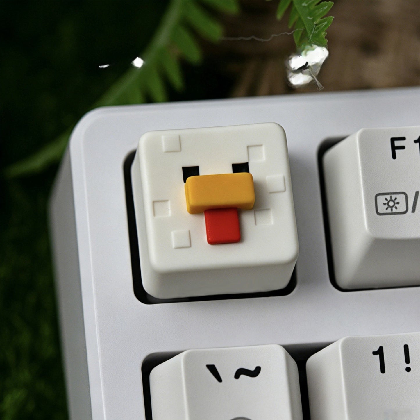 Keycapper™ Minecraft Cube Series Artisanal Keycap – A focused macro image of a white 3D voxel Chicken mob head novelty keycap, with a yellow beak and red wattle, replacing the F1 key on a white and grey mechanical keyboard.